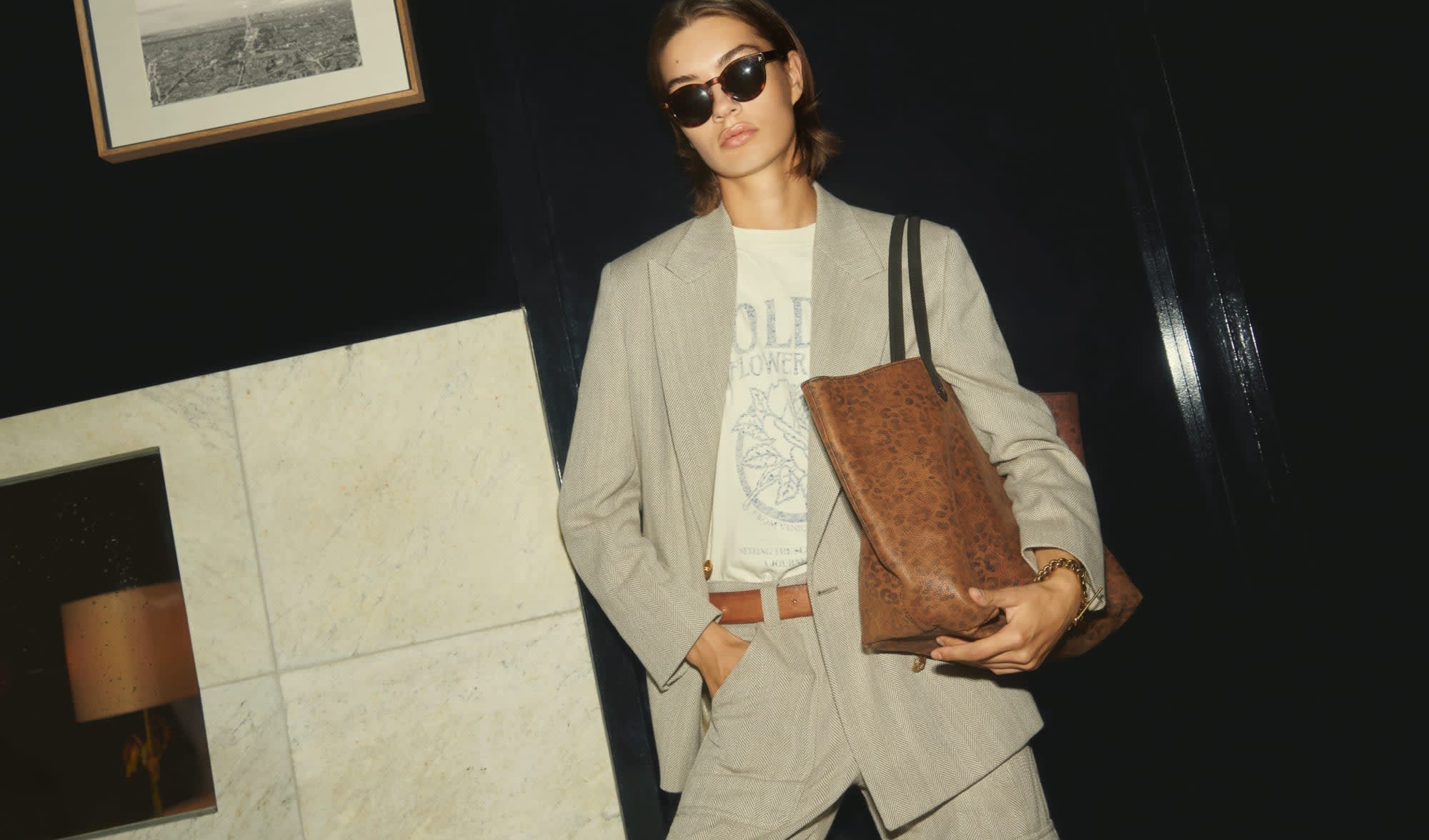 short-hair-woman-with-sunglasses-wearing-white-t-shirt-and-beige-suit-holding-brown-handbag