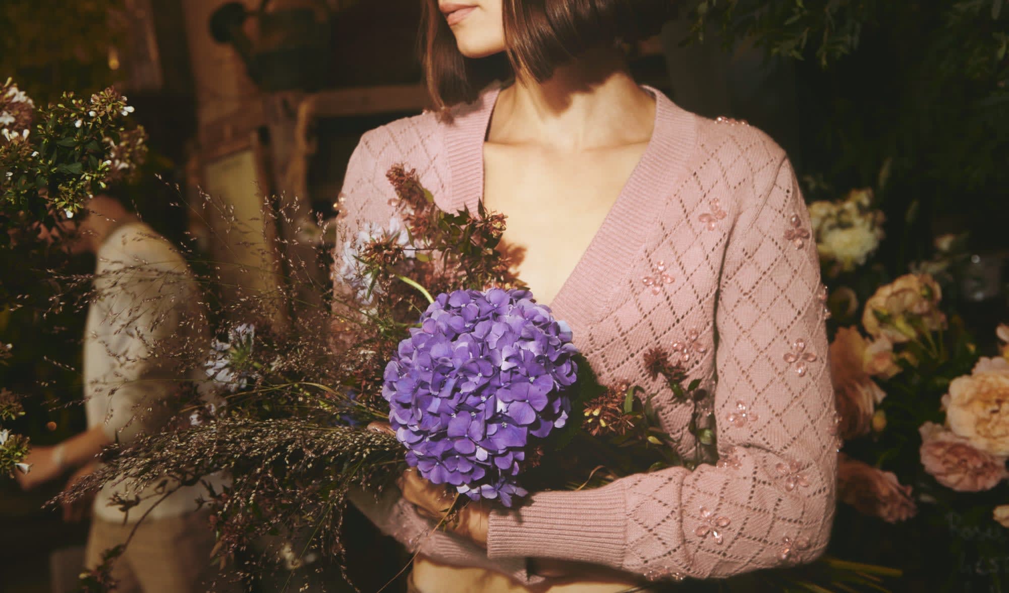 woman-wearing-pink-knitted-cardigan-holding-violet-flowers
