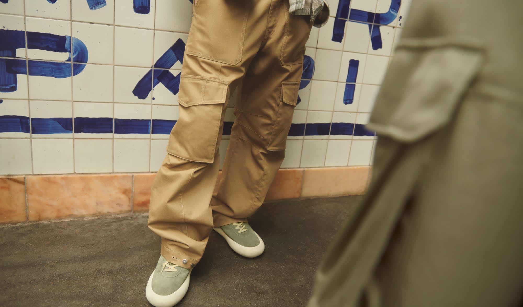 Man-wearing-cargo-trousers-in-khaki-cotton-in-front-of-a-tiled-wall