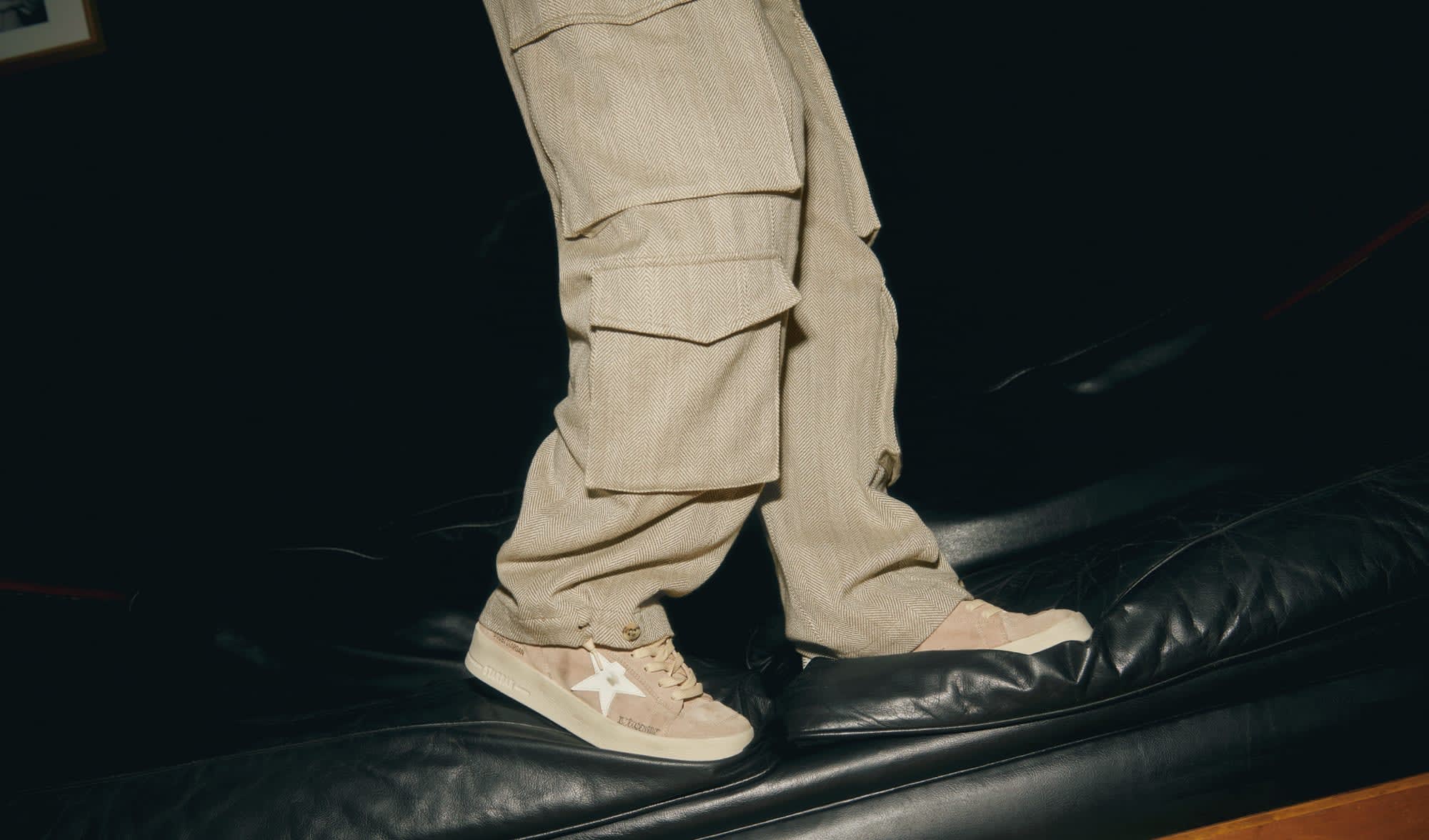 beige-cargo-pants-and-beige-stardan-sneakers-standing-on-black-leather-sofa