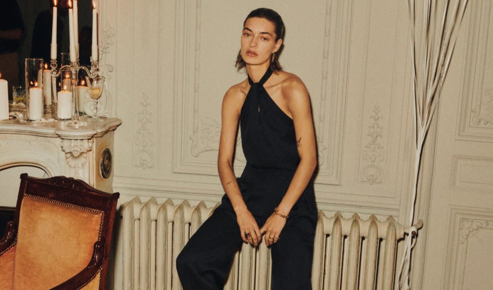 woman-with-short-hair-in-black-jumsuit-sitting-on-radiator-in-victorian-style-house