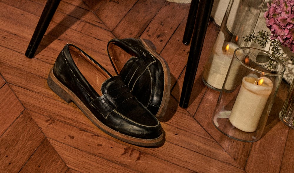 black-loafers-with-brown-soles-next-to-white-candle-on-wooden-parquet-floor