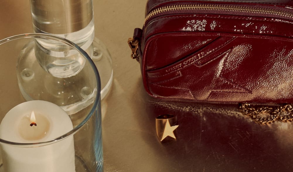 bordeaux-mini-star-bag-behind-ring-with-golden-goose-logo-and-white-candle-on-the-side
