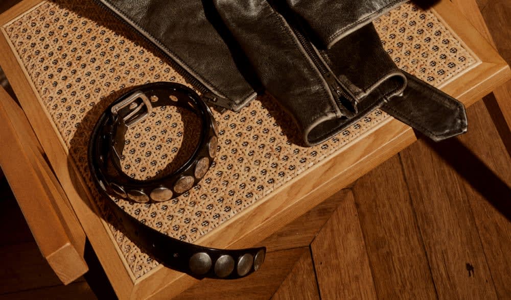 black-leather-jacket-and-belt-with-metallic-details-on-brown-and-beige-interwined-chair