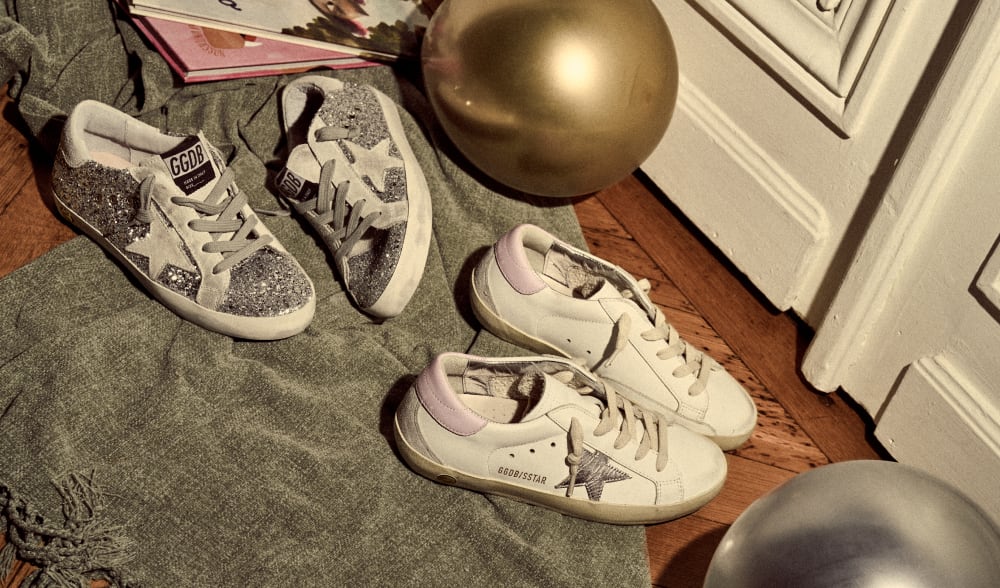 silver-glittered-super-star-and-white-super-star-sneakers-with-pink-heel-on-grey-blanket-on-wooden-floor-in-front-of-gold-balloon