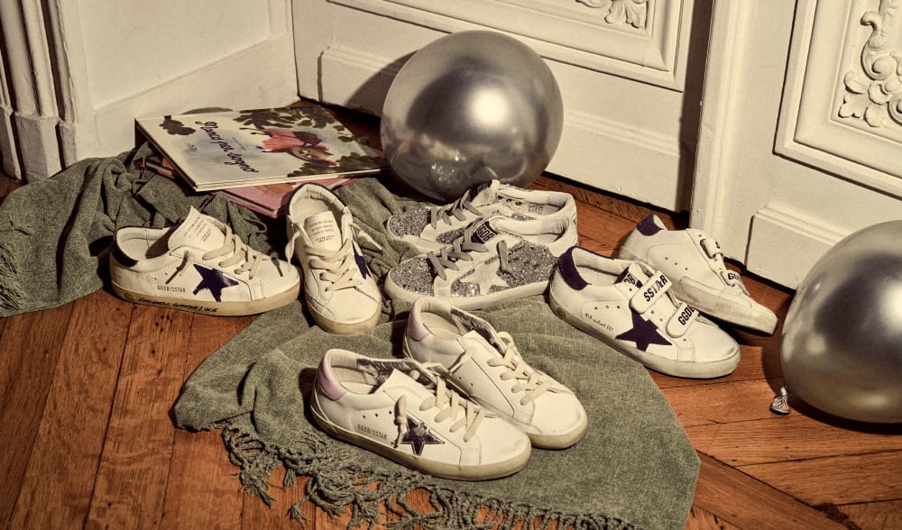 silver-glittered-super-star-and-three-white-super-star-sneakers-with-black-star-on-grey-blanket-on-wooden-floor-in-front-of-silver-balloon